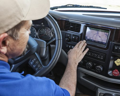 Driver parked by the side of the road using a GPS mapping device in the cab of a commercial truck.
